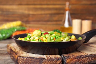 Photo of Frying pan with mix of frozen vegetables on wooden board