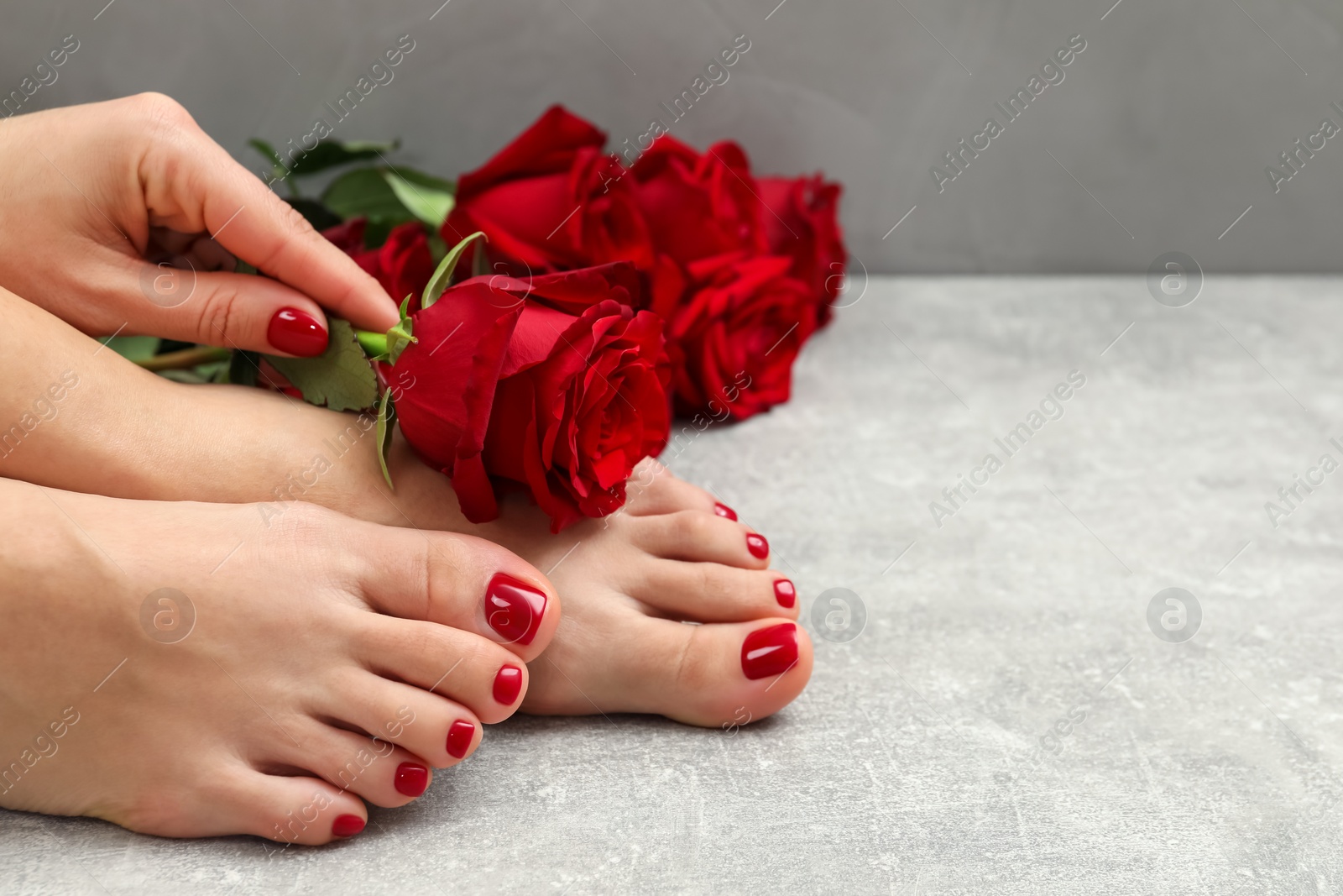 Photo of Woman with stylish red toenails after pedicure procedure and rose flowers on grey textured floor, closeup. Space for text