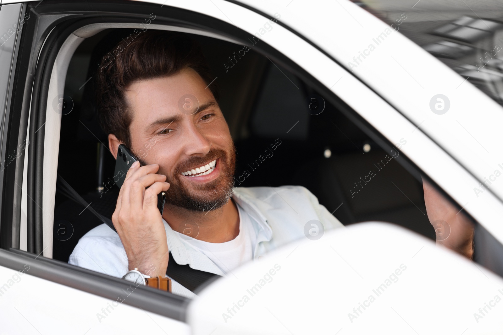 Photo of Happy bearded man talking on smartphone in car, view from outside