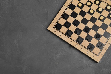 Photo of Wooden checkerboard with game pieces on grey table, top view. Space for text