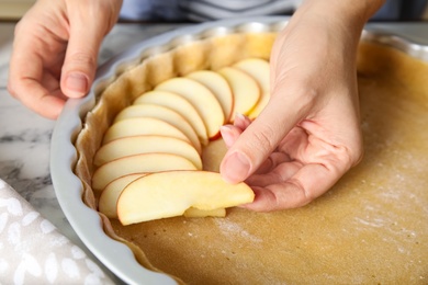 Woman putting apple slice into baking dish with dough to make traditional English pie at table, closeup