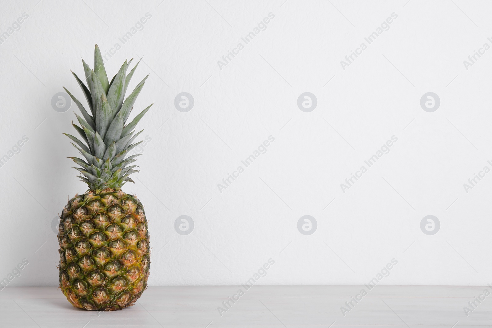 Photo of Whole ripe pineapple on white wooden table. Space for text