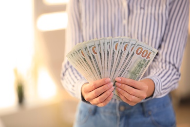 Young woman holding dollar bills on blurred background, closeup