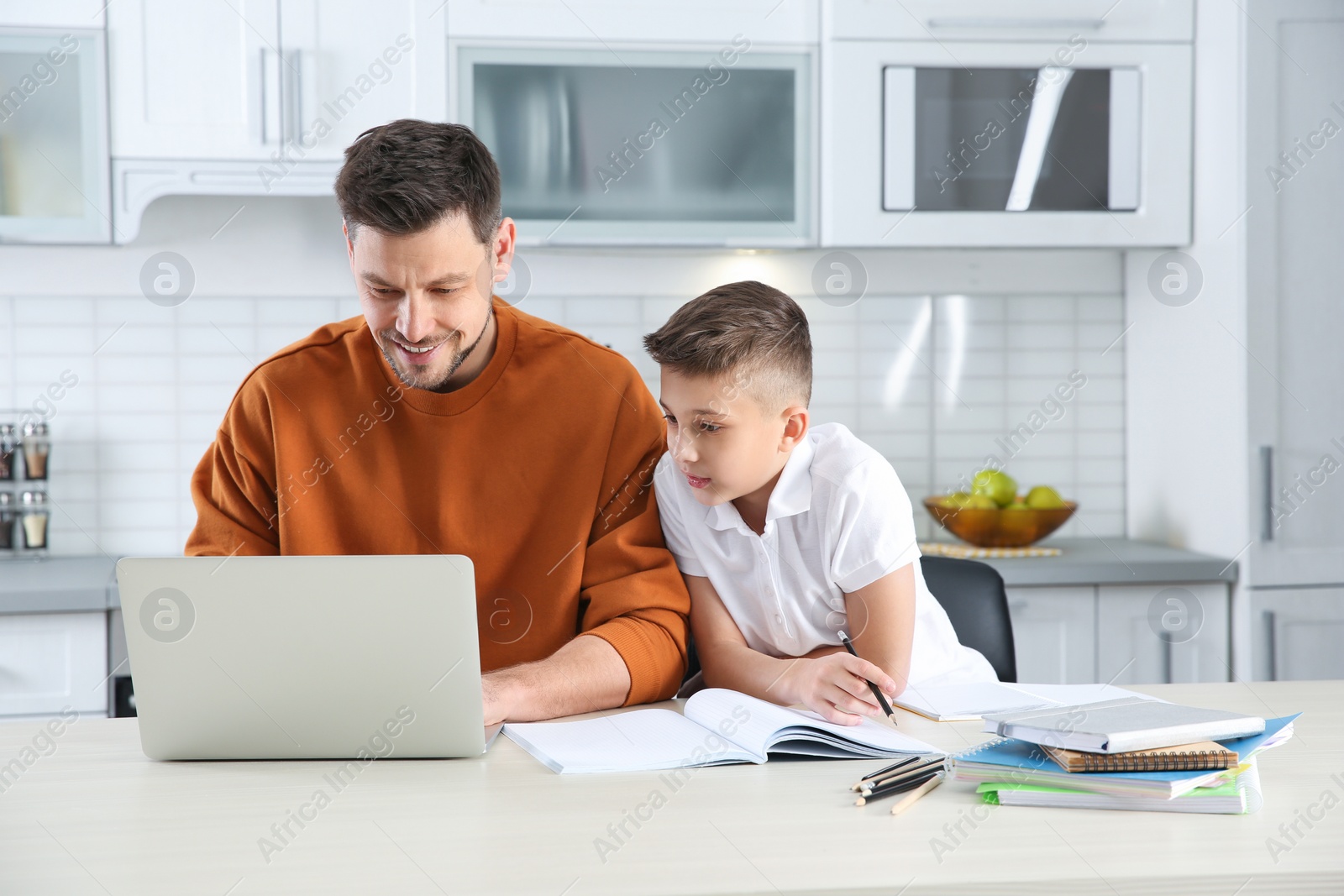 Photo of Dad helping his son with homework in kitchen