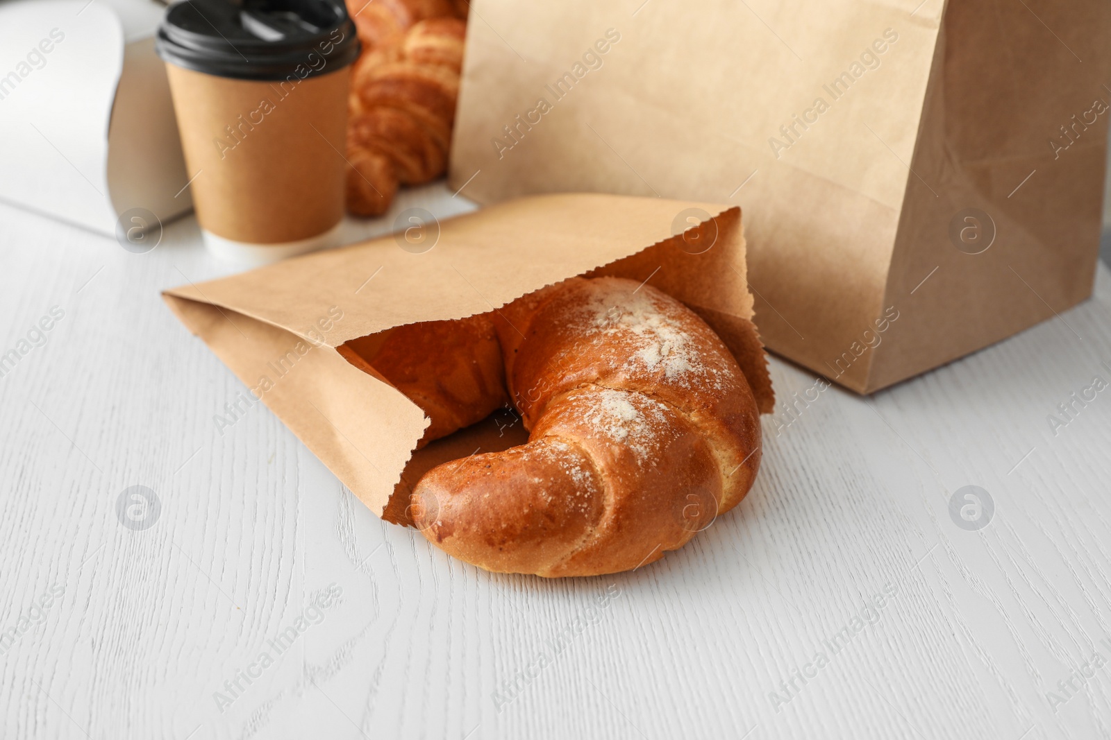 Photo of Paper bag with pastry and takeaway food on wooden table