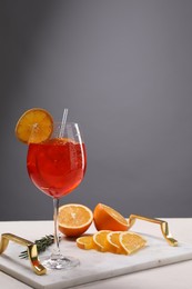 Photo of Glass of tasty Aperol spritz cocktail with orange slices and rosemary on white table against gray background, space for text