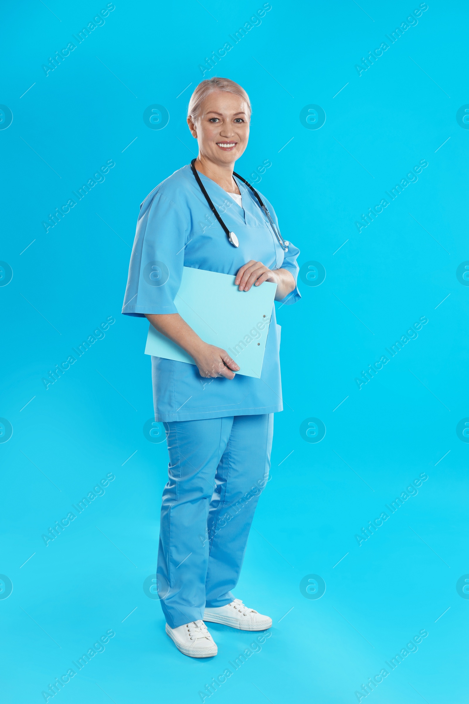 Photo of Mature doctor with stethoscope and clipboard on blue background