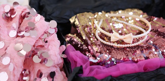 Photo of Headbands and stylish pink carnival costume with sequins in black box, closeup