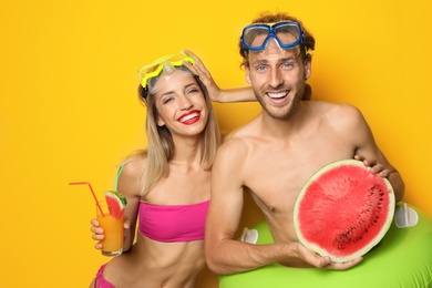 Photo of Happy young couple in beachwear with inflatable ring and cocktail on color background