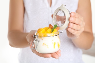 Photo of Woman holding glass jar of tasty peach dessert with yogurt, closeup