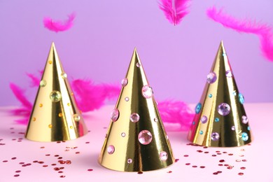 Photo of Golden party hats with bright rhinestones, confetti and feathers on color background