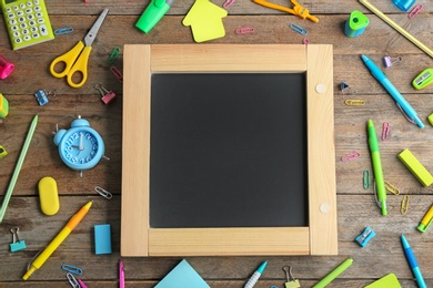 Different school stationery and blank small chalkboard on wooden background, flat lay. Space for text