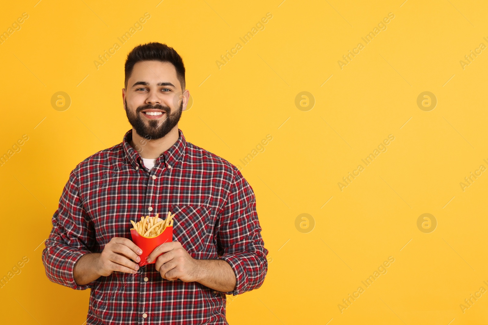 Photo of Young man with French fries on orange background, space for text