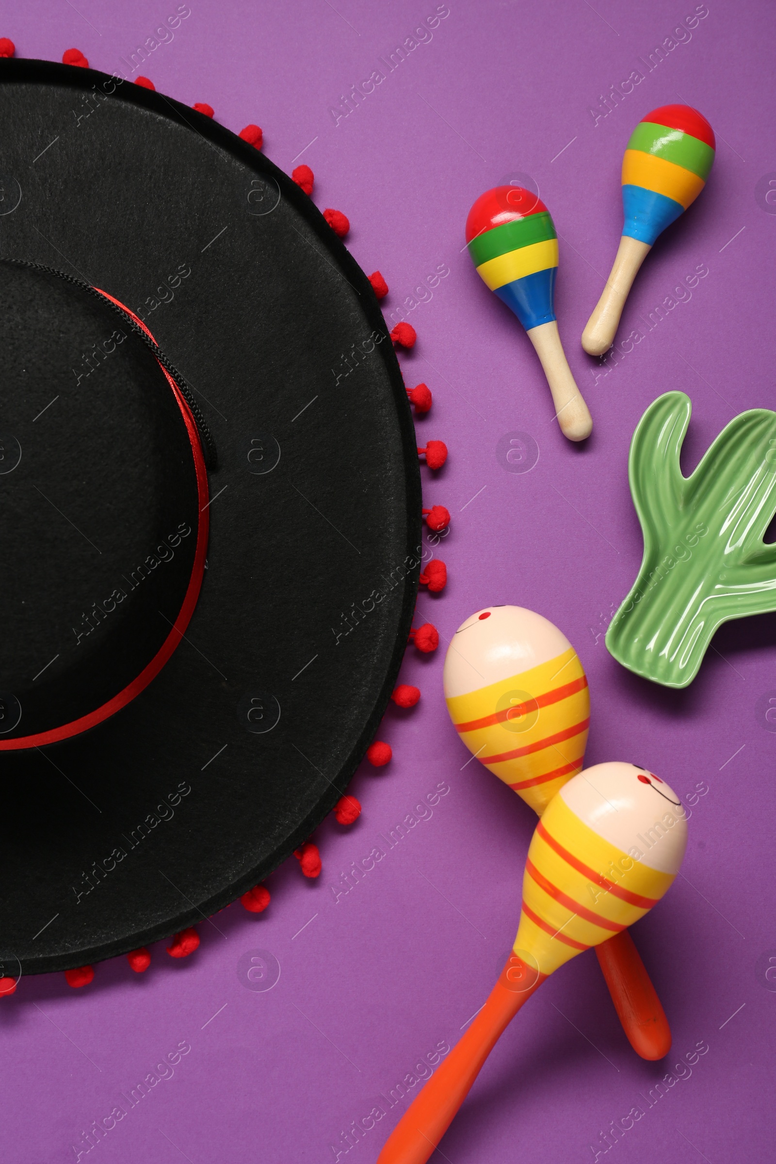 Photo of Mexican sombrero hat, maracas and toy cactus on purple background, flat lay