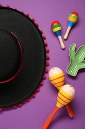 Mexican sombrero hat, maracas and toy cactus on purple background, flat lay