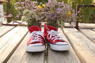 Photo of Shoes with beautiful flowers on deck outdoors