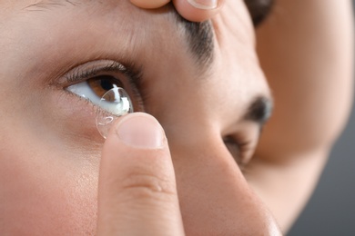 Young man putting contact lens into his eye, closeup