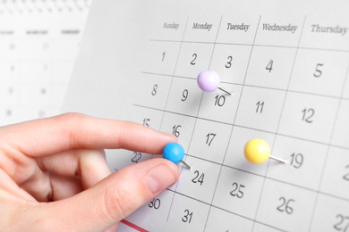 Photo of Woman marking date in calendar with drawing pin, closeup