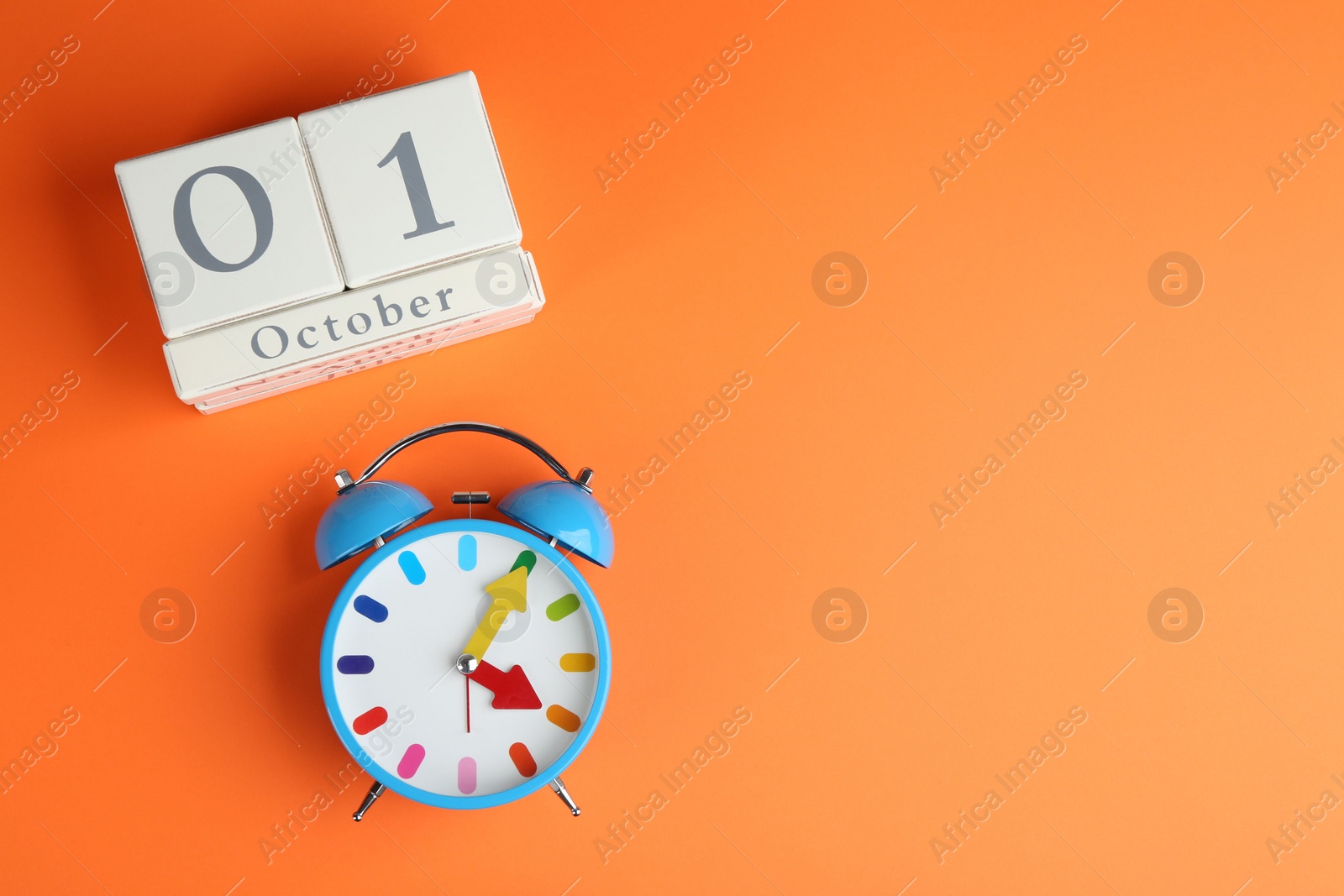Photo of Wooden block calendar and alarm clock on orange background, flat lay. Space for text