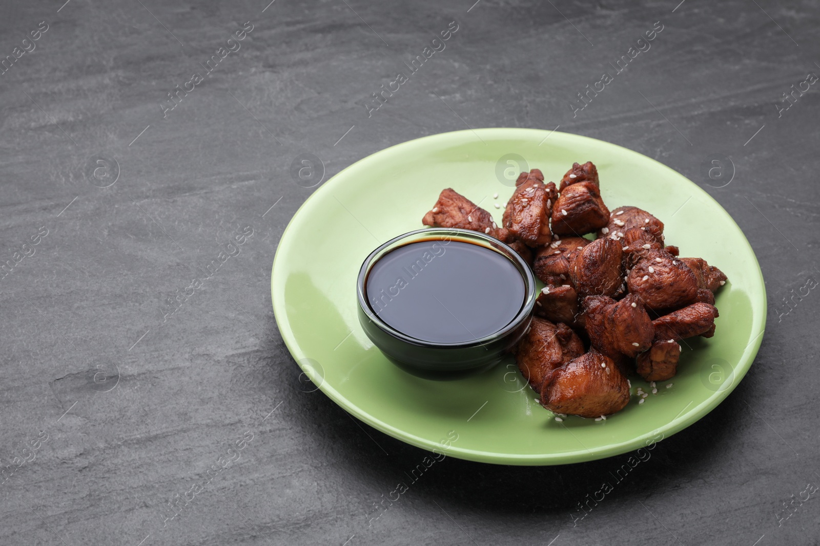 Photo of Tasty roasted meat served with soy sauce on dark grey table. Space for text