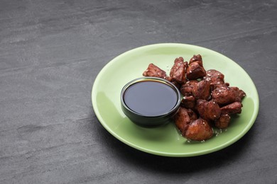 Tasty roasted meat served with soy sauce on dark grey table. Space for text