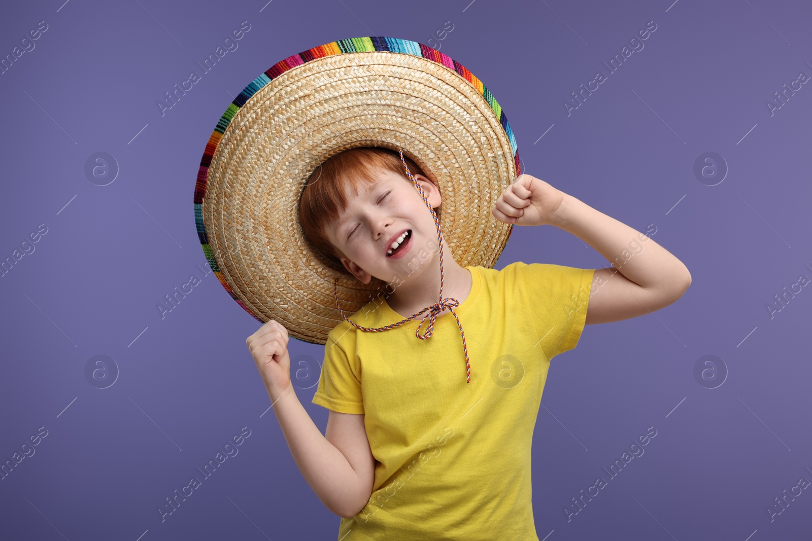 Photo of Cute boy in Mexican sombrero hat dancing on violet background