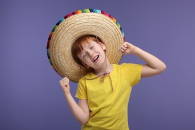 Photo of Cute boy in Mexican sombrero hat dancing on violet background