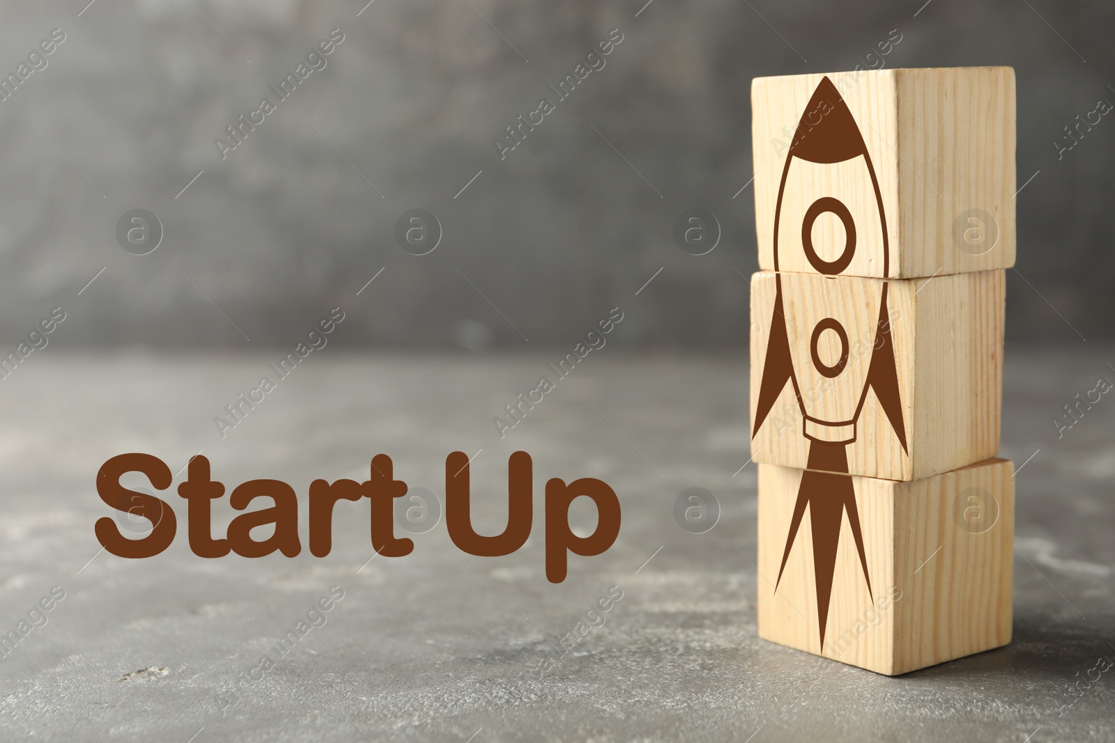 Image of Rocket made of wooden cubes and text START UP on grey background