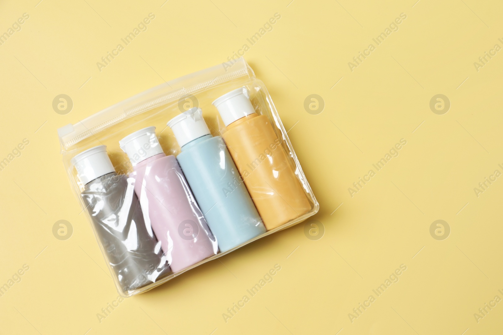 Photo of Cosmetic travel kit in plastic bag on yellow background, top view. Space for text