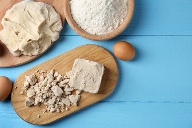 Photo of Compressed yeast, eggs, dough and flour on light blue wooden table, flat lay. Space for text