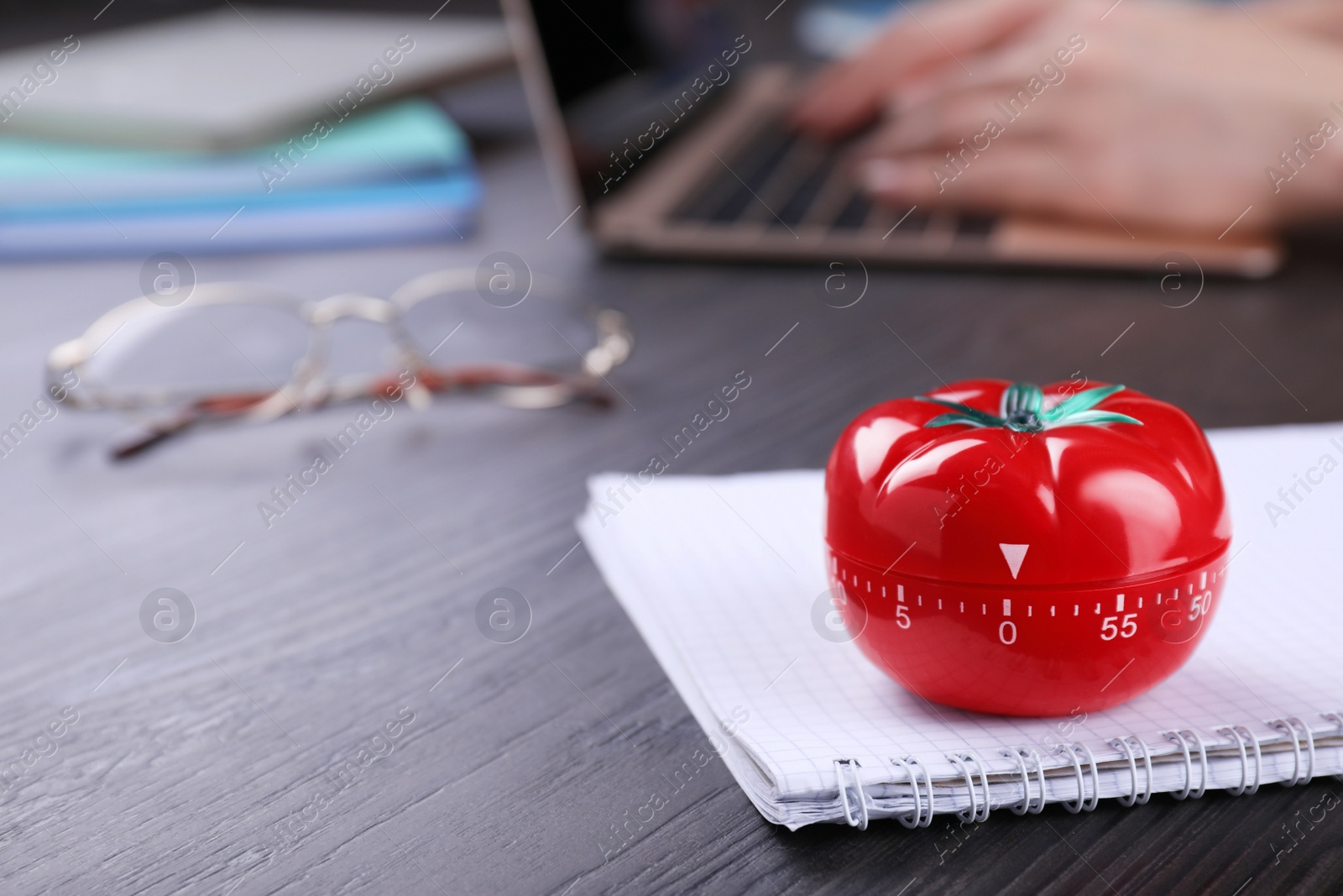 Photo of Woman working on laptop at wooden table, focus on kitchen timer in shape of tomato. Space for text