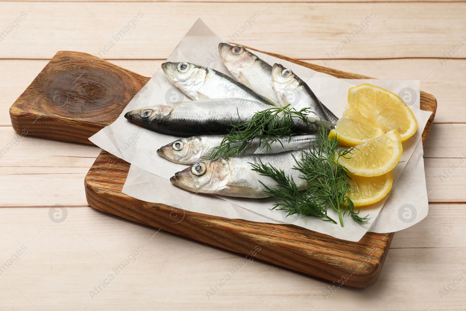 Photo of Fresh raw sprats, lemon and dill on light wooden table