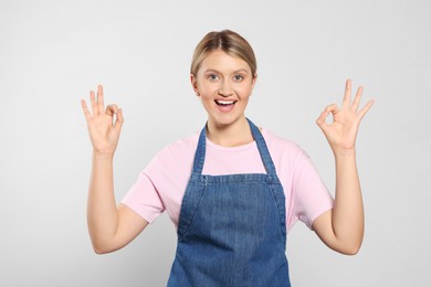 Photo of Beautiful young woman in denim apron on light grey background