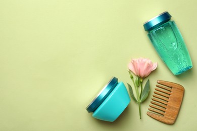 Hair care cosmetic products, wooden comb and flower on light green background, flat lay. Space for text
