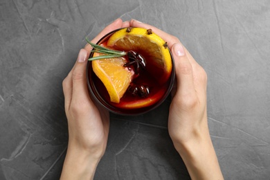 Young woman holding glass with tasty mulled wine at grey table, top view