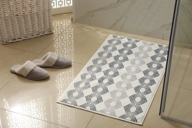 Photo of Soft bath mat and slippers on floor indoors