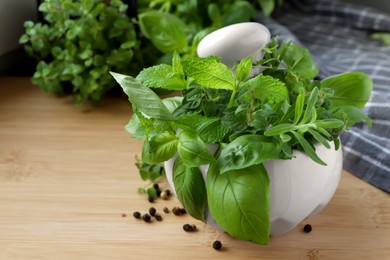 Mortar with different fresh herbs and black peppercorns on wooden table, closeup