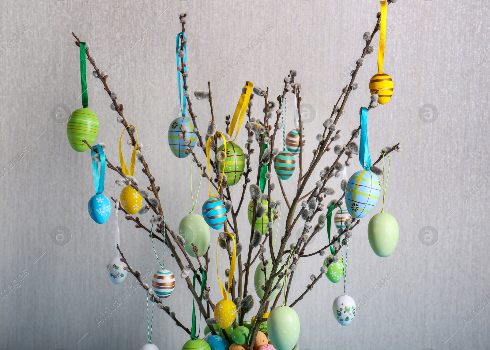 Photo of Beautiful willow branches with painted eggs on light grey background, closeup. Easter decor