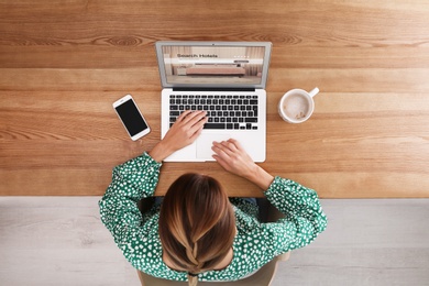 Image of Woman searching hotel using laptop at table, top view. Booking online service