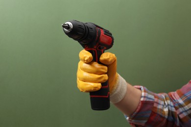Photo of Handyman holding electric screwdriver on pale green background, closeup