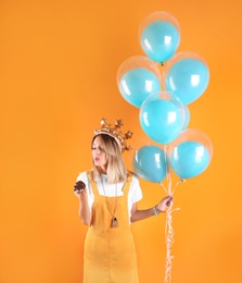 Photo of Young woman with birthday muffin and air balloons on color background