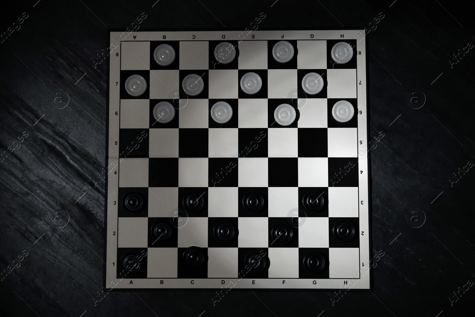 Photo of Checkerboard with game pieces on black table, top view