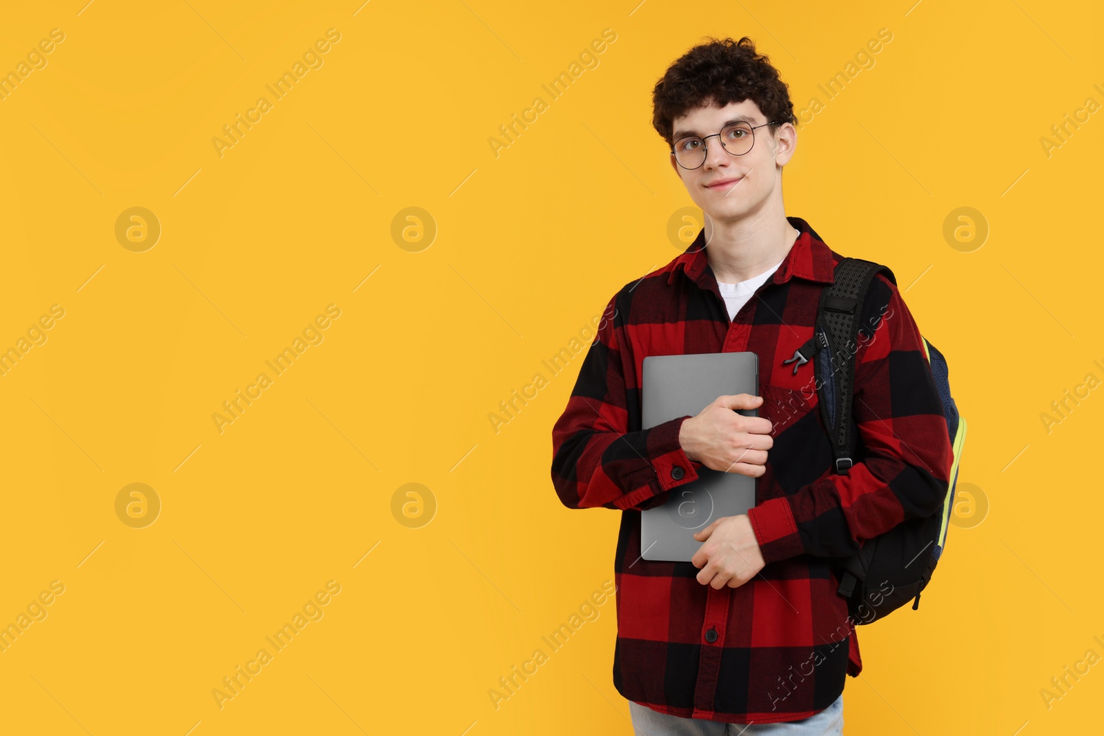Photo of Portrait of student with backpack, laptop and glasses on orange background. Space for text