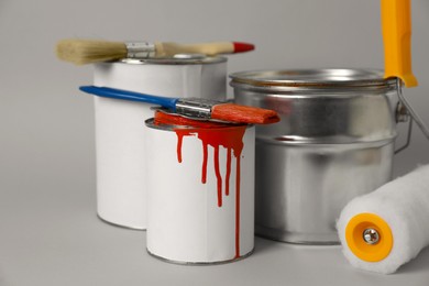 Photo of Cans of orange paint, brushes and roller on grey background