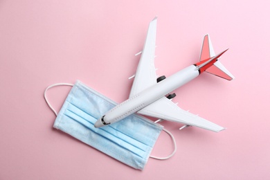 Photo of Toy airplane and protective mask on pink background, flat lay. Travelling during coronavirus pandemic