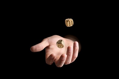 Man throwing golden dice on black background, closeup