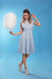 Full length portrait of pretty young woman with tasty cotton candy on blue background