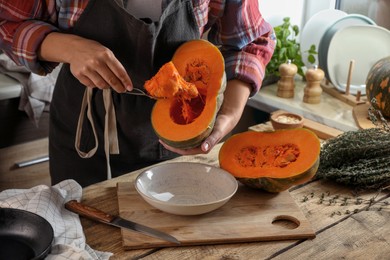 Photo of Woman removing seeds from raw pumpkin at wooden table in kitchen, closeup