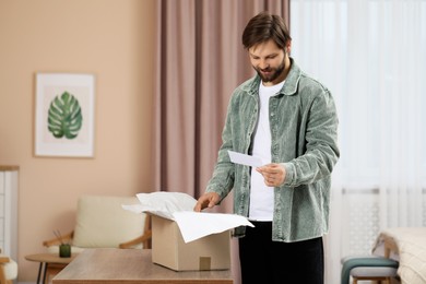 Photo of Happy man with greeting card near parcel at home. Internet shopping