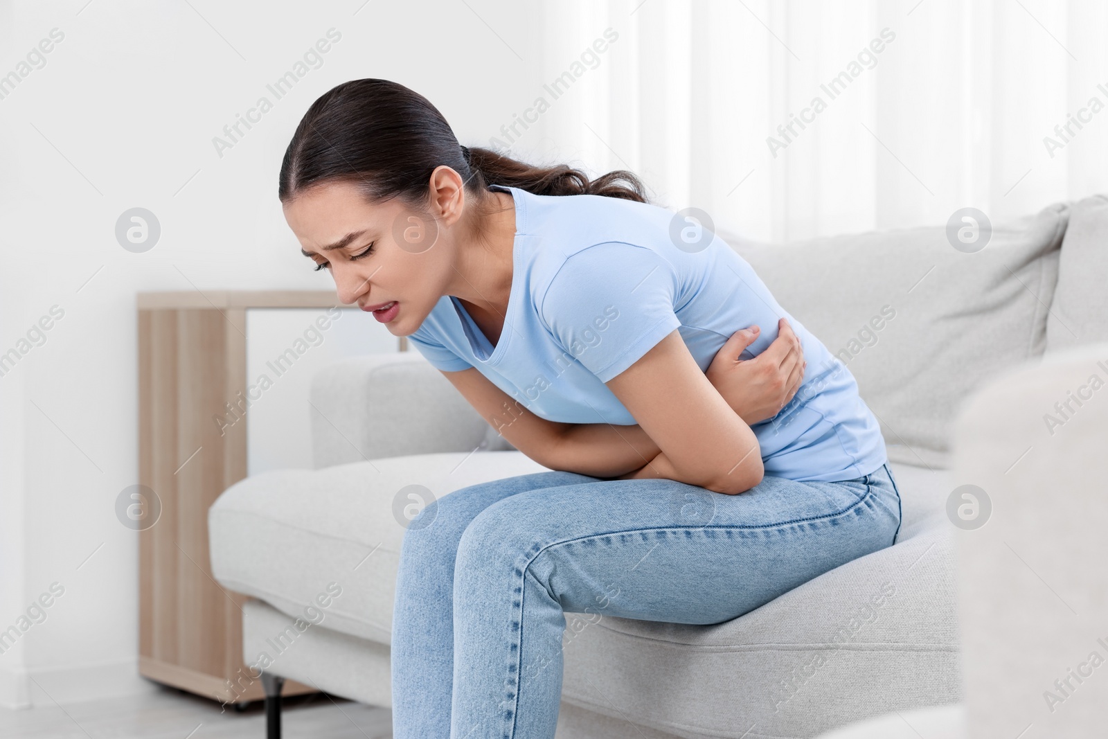 Photo of Woman suffering from abdominal pain on sofa at home. Unhealthy stomach